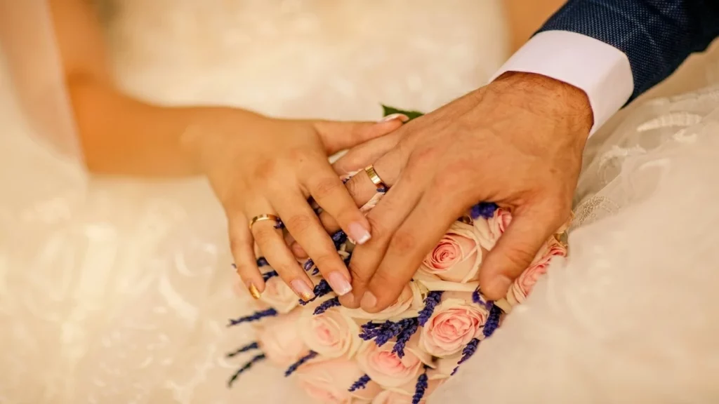 Pareja de novios con alianzas de boda clásicas sobre ramo nupcial en Joyería Mikel Bilbao